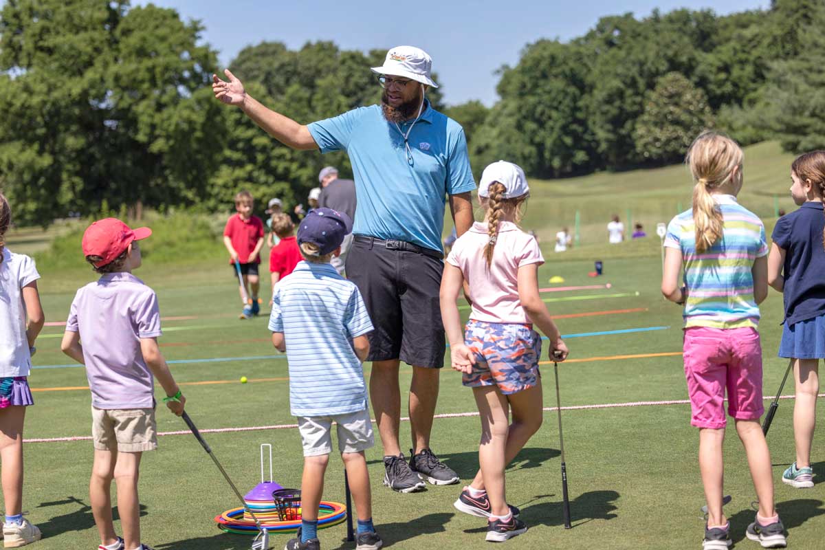 Golf instructor teaching young kids with various learning apparatuses.
