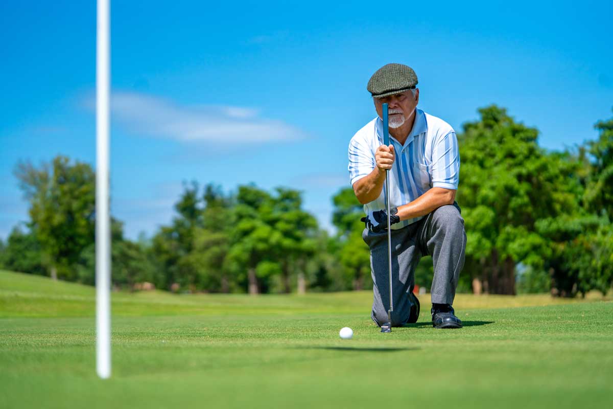 Senior golfer kneeling on green to line up a putt.